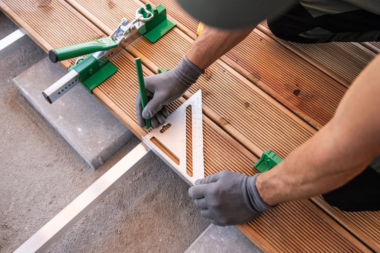 A craftsman carefully places a square tool on wooden planks during a deck renovation outdoors