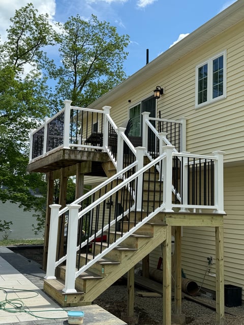 Exterior staircase with white railings leading to an elevated deck on a beige siding house with green shutters