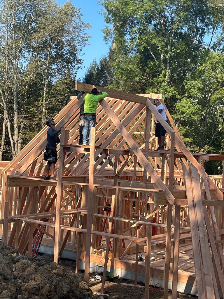 Workers constructing wooden frame of a house with trees in background