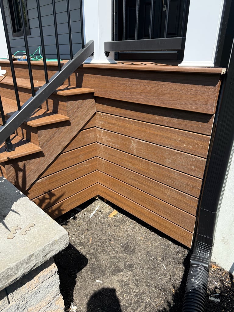 Wooden deck stairs with metal railing leading up to a black-framed glass door entrance on a modern home