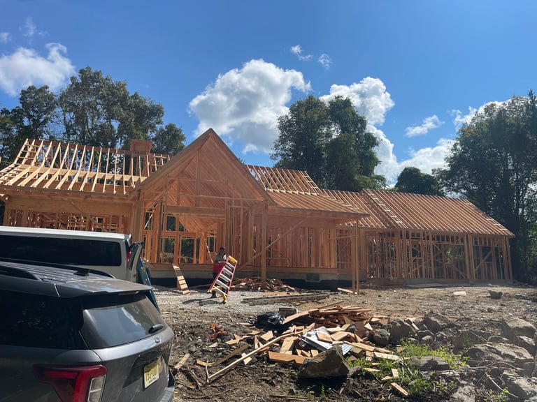 New construction wooden frame buildings under development with a vehicle parked in front, blue sky and trees in background
