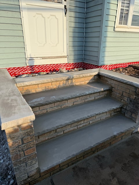 Concrete and brick outdoor steps with red roof flashing, white door, and light blue siding visible in background