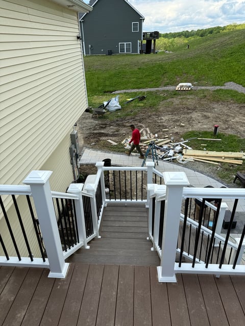 Elevated deck with white railings overlooking a backyard with houses, rolling green hills, and a person with a bicycle below